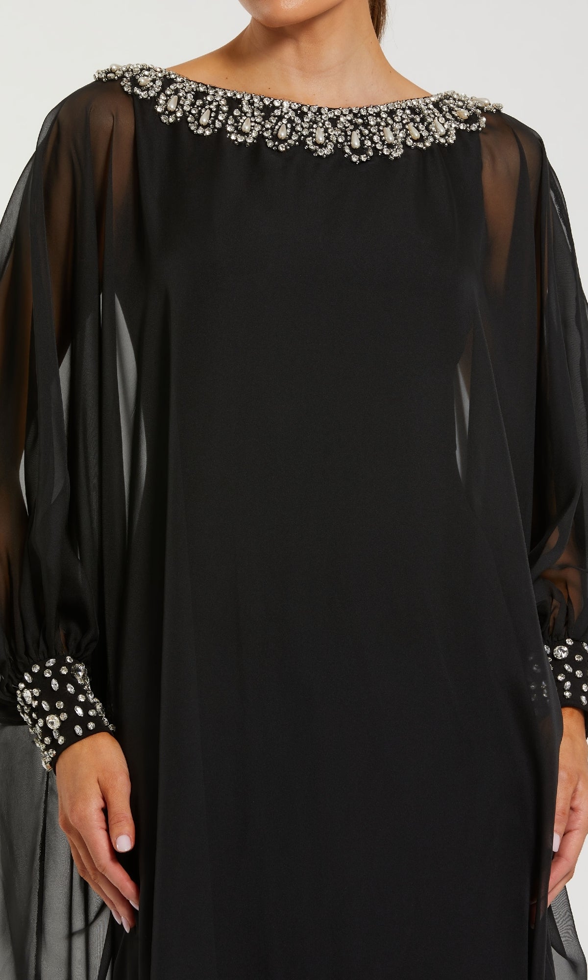 A woman models the Mac Duggal 56203 long formal dress, a black chiffon gown featuring sheer long sleeves, a rhinestone-embellished neckline, and sparkling beaded cuffs, shown from shoulders to mid-thigh.